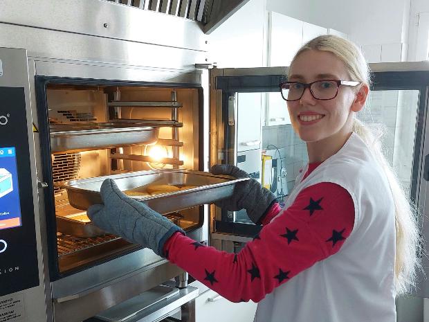 Selina Zimmermann hat als Hauswirtschaftshelferin im Haus Eulenhorst ihren Traumberuf gefunden. Die Förderung der Aktion Arbeit ermöglicht ihr langfristige Teilhabe am Arbeitseben. (c) Caritasverband Koblenz/Marco Wagner Frau an einem Backofen