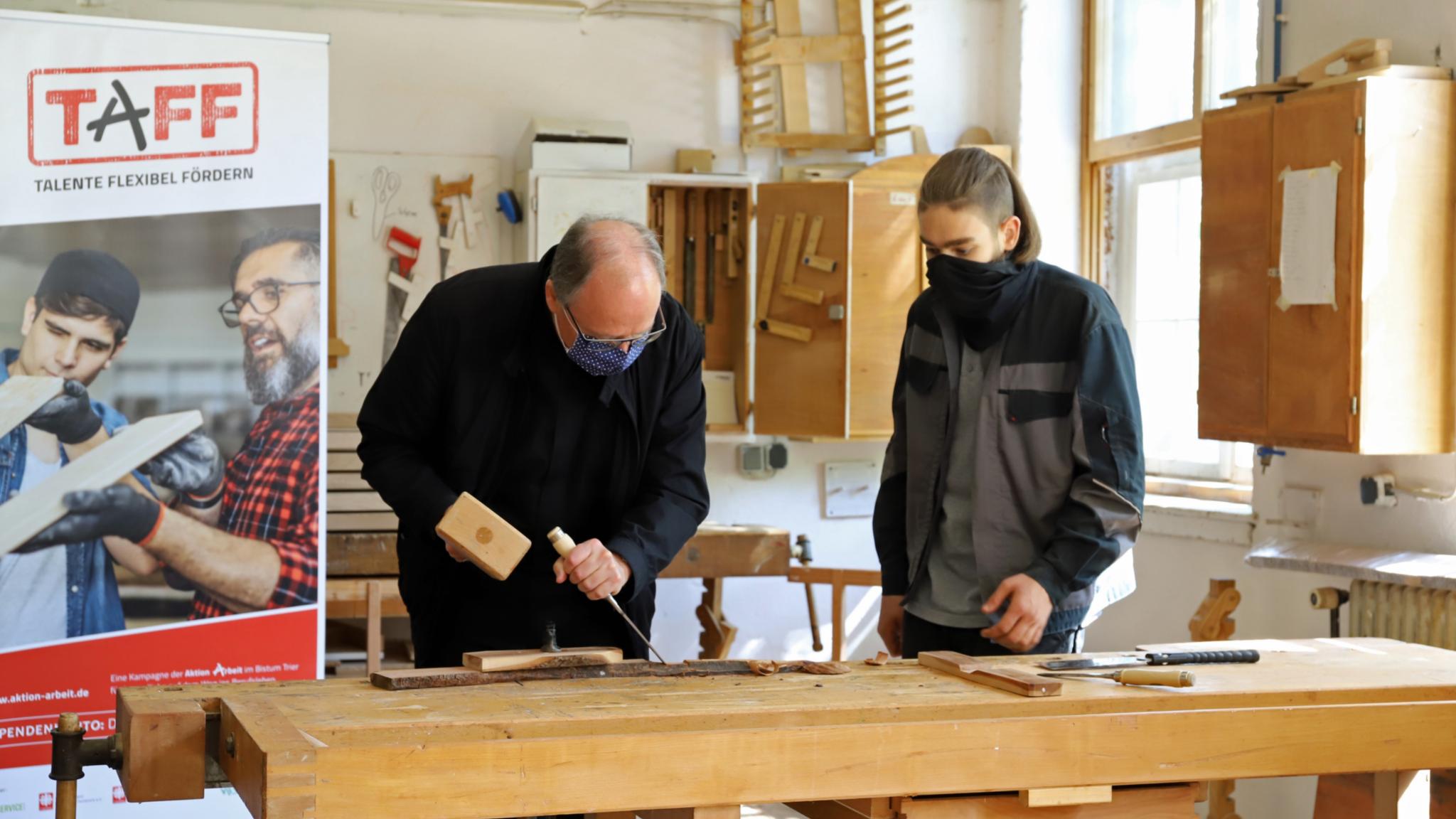 Bischof Ackermann und Marlon schreinern gemeinsam ein Holzkreuz.